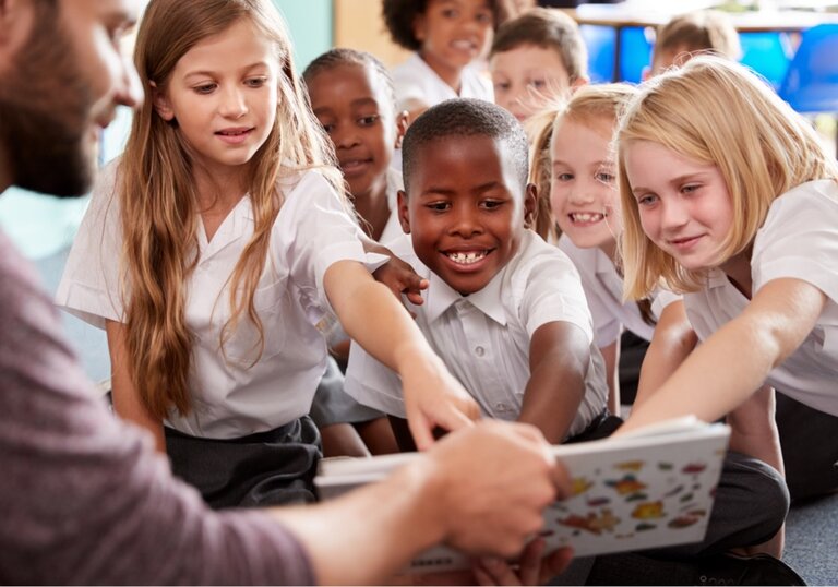 Lesestunde mit Kindern Gruppe von Schülerinnen und Schülern im Unterricht, die begeistert auf ein Bilderbuch zeigen und es gemeinsam mit einem Lehrer anschauen.