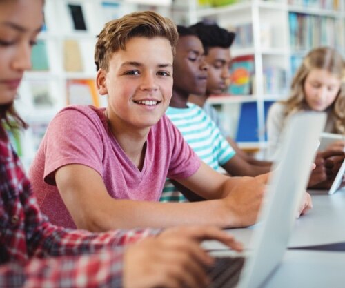 Schüler beim Lernen am Computer Schülergruppe in einem Klassenzimmer, die an Laptops arbeitet. Ein Junge lächelt in die Kamera, während andere konzentriert tippen.