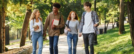 Freunde beim Spaziergang im Park Schülerinnen und Schüler gehen gemeinsam einen Weg im Grünen, lachen und unterhalten sich, während sie Bücher und Notizen tragen.